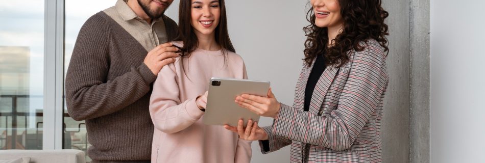 Corretora de imóveis mostra informações em um tablet a um casal sorridente dentro de um apartamento